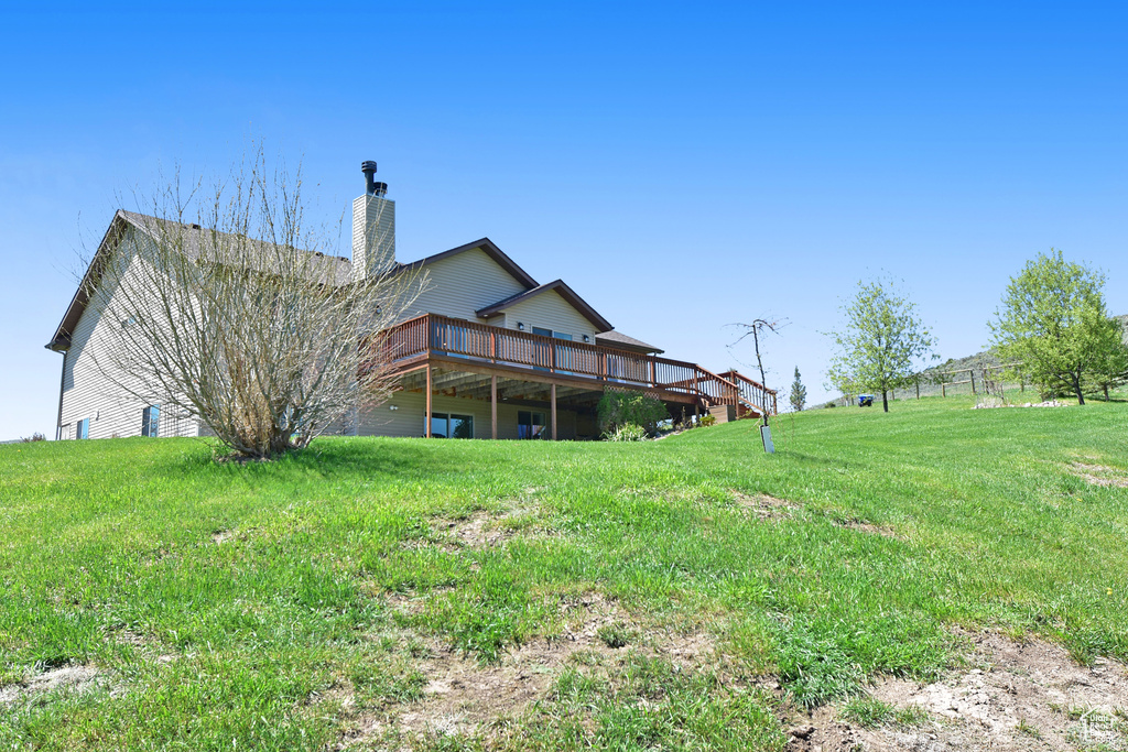 Rear view of house with a deck, a chimney, and a lawn