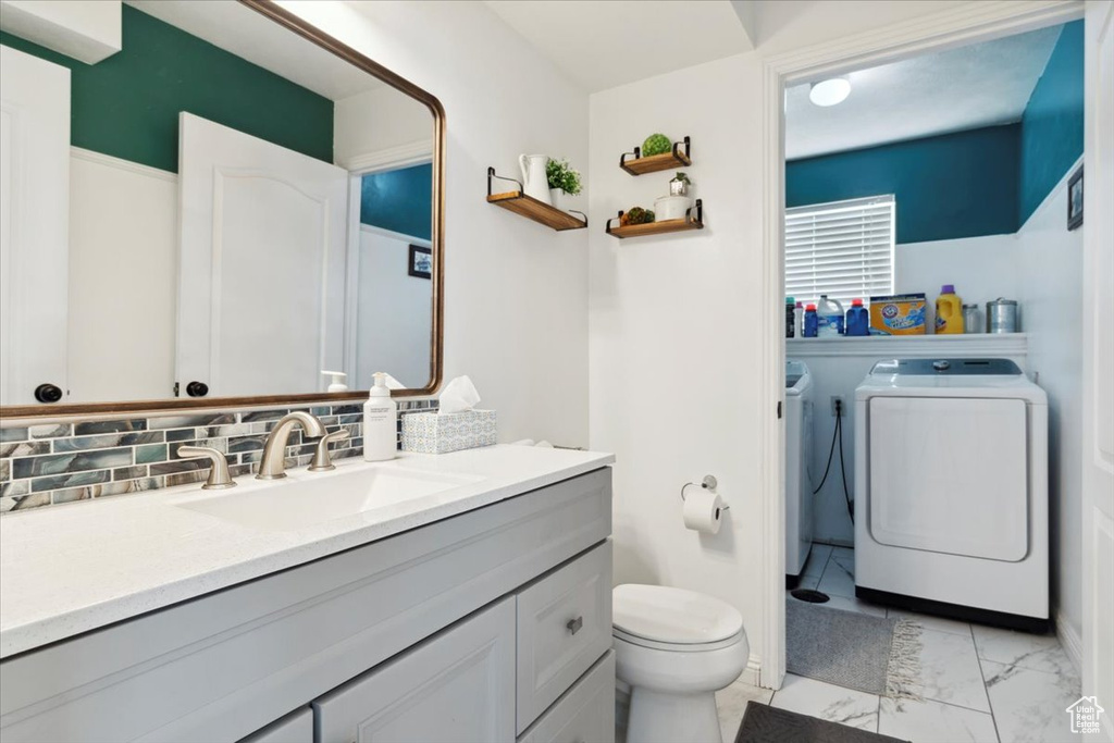 Bathroom with independent washer and dryer, toilet, vanity, marble look tiles, and backsplash