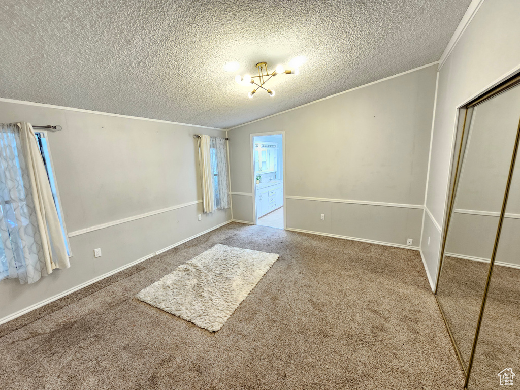 Unfurnished bedroom with crown molding, a textured ceiling, a closet, carpet floors, and a chandelier