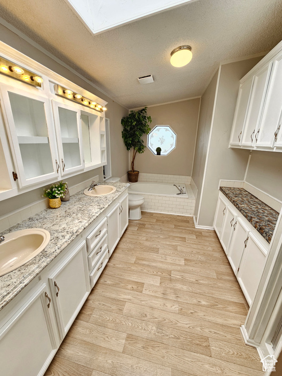 Bathroom featuring double vanity, a garden tub, wood finished floors, toilet, and a textured ceiling
