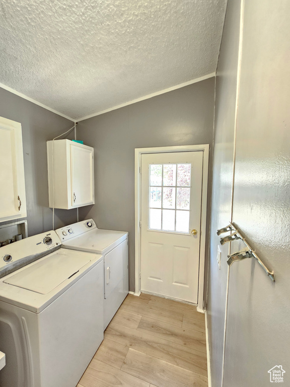 Laundry area with cabinet space, separate washer and dryer, light wood-style floors, a textured ceiling, and crown molding