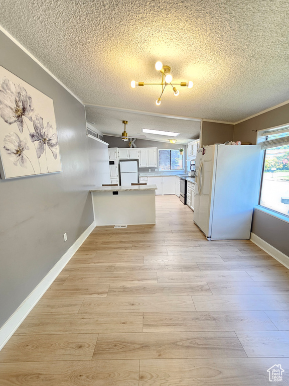 Kitchen with a textured ceiling, a peninsula, freestanding refrigerator, baseboards, and light wood-style floors