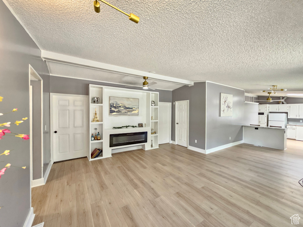 Unfurnished living room featuring a textured ceiling, baseboards, a glass covered fireplace, light wood finished floors, and ceiling fan