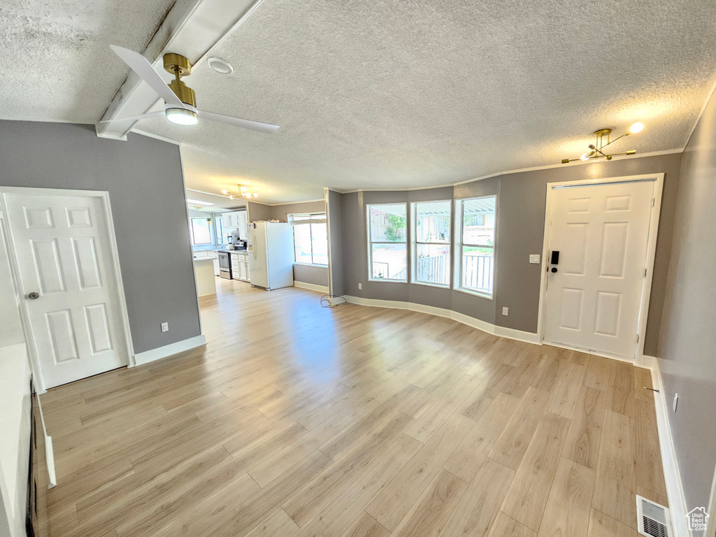 Unfurnished living room with ceiling fan, light wood-style floors, baseboards, a textured ceiling, and beamed ceiling