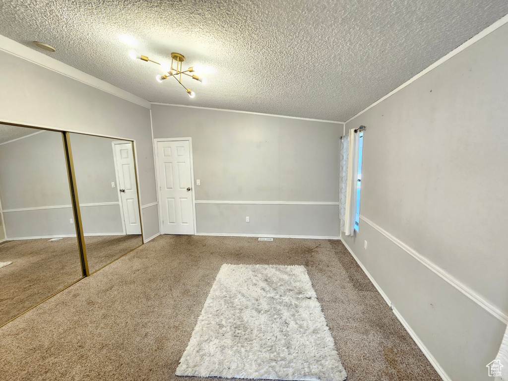 Unfurnished bedroom featuring a textured ceiling, carpet flooring, ornamental molding, a closet, and lofted ceiling
