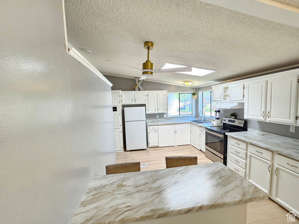 Kitchen with freestanding refrigerator, stainless steel electric stove, a sink, white cabinets, and a textured ceiling