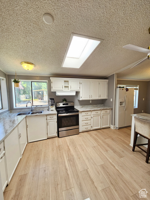 Kitchen featuring stainless steel range with electric stovetop, white fridge with ice dispenser, a sink, under cabinet range hood, and a textured ceiling