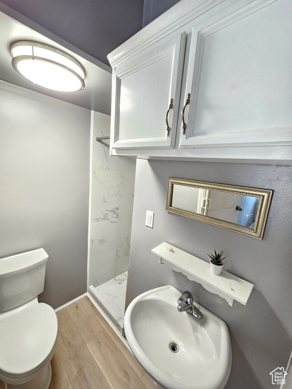 Bathroom featuring a sink, a shower stall, toilet, wood finished floors, and baseboards