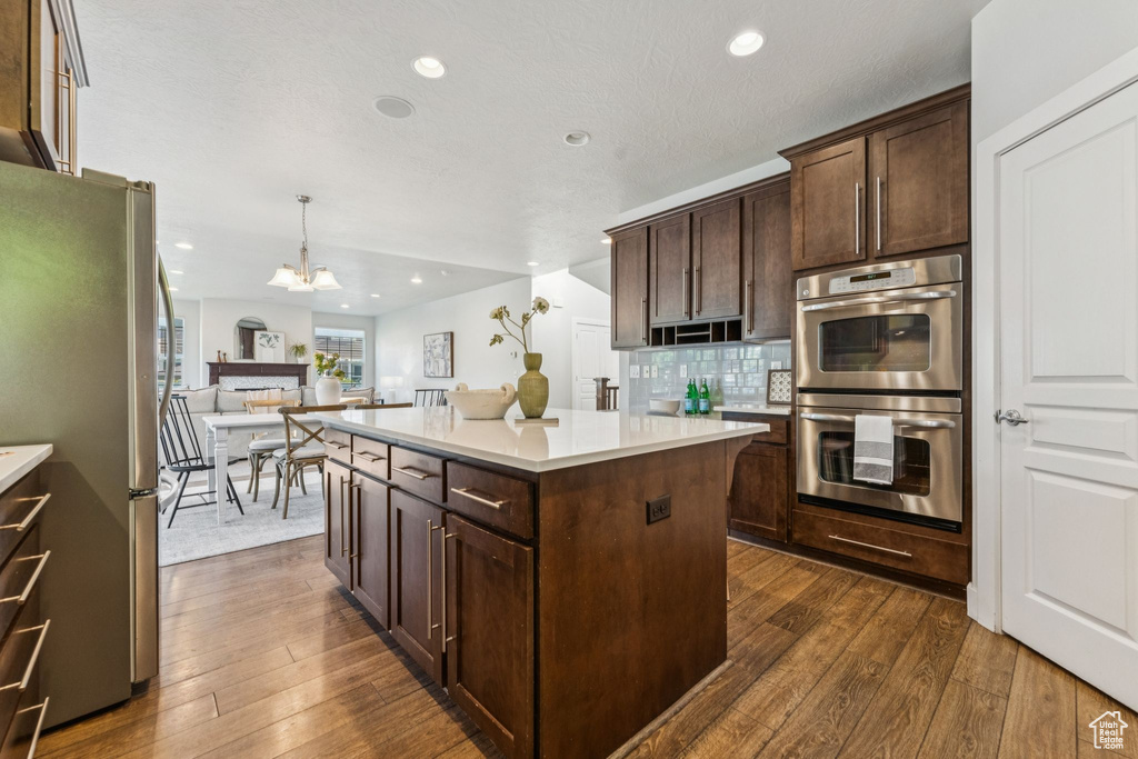 Kitchen featuring appliances with stainless steel finishes, light countertops, a kitchen island, a chandelier, and dark brown cabinets