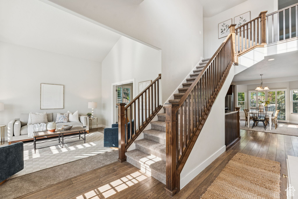 Stairway with high vaulted ceiling, hardwood / wood-style flooring, a chandelier, and baseboards
