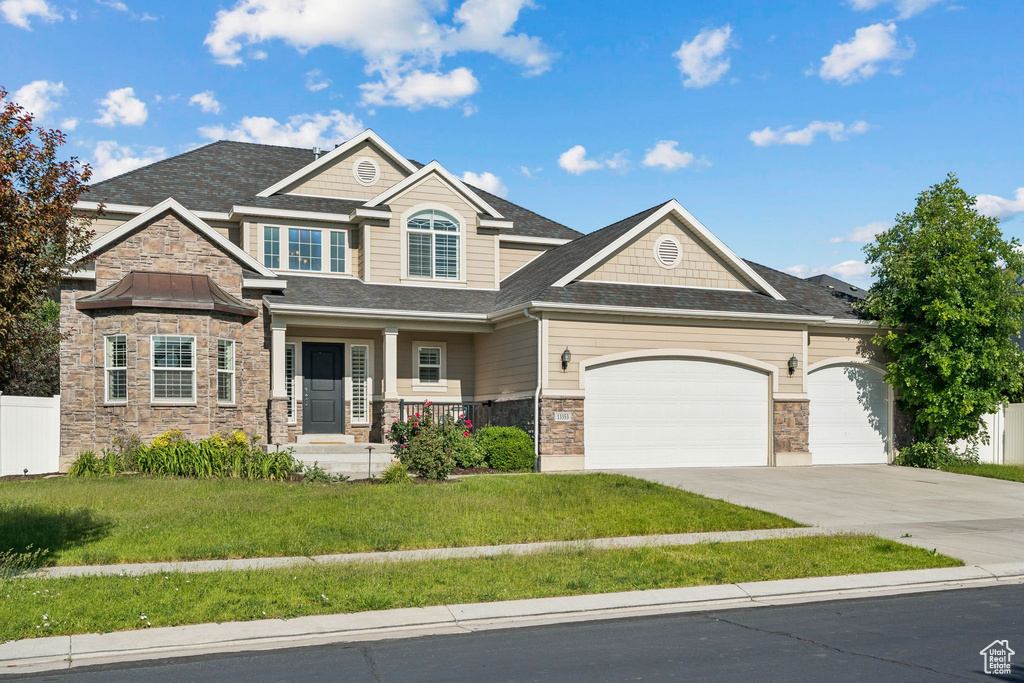 Craftsman house with stone siding, a porch, a front lawn, concrete driveway, and a garage