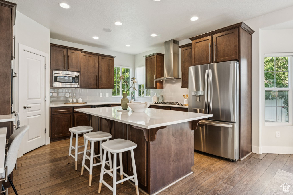 Kitchen featuring appliances with stainless steel finishes, wall chimney range hood, healthy amount of natural light, a kitchen island, and recessed lighting