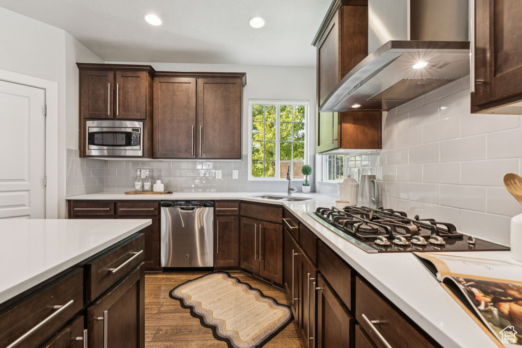 Kitchen with stainless steel appliances, wall chimney range hood, a sink, light countertops, and recessed lighting