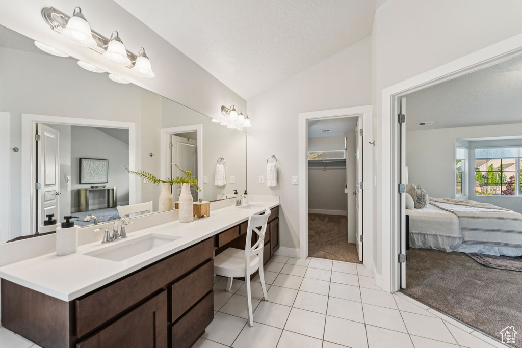 Bathroom with vaulted ceiling, double vanity, tile patterned floors, ensuite bath, and baseboards