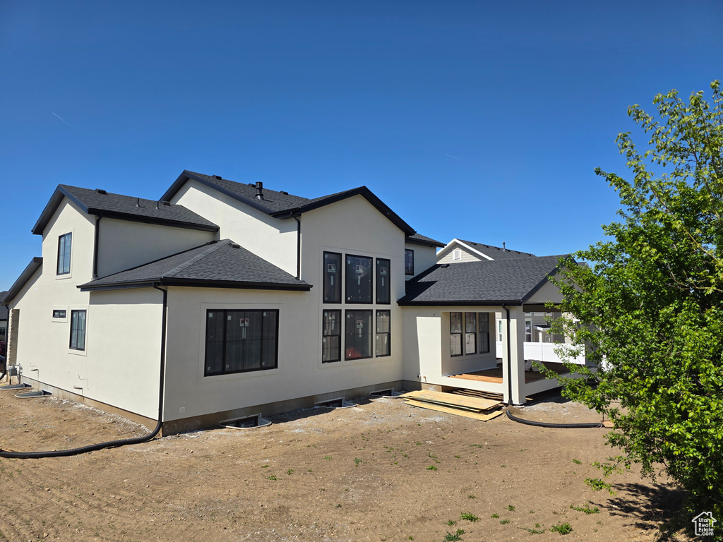 Back of property with stucco siding and roof with shingles