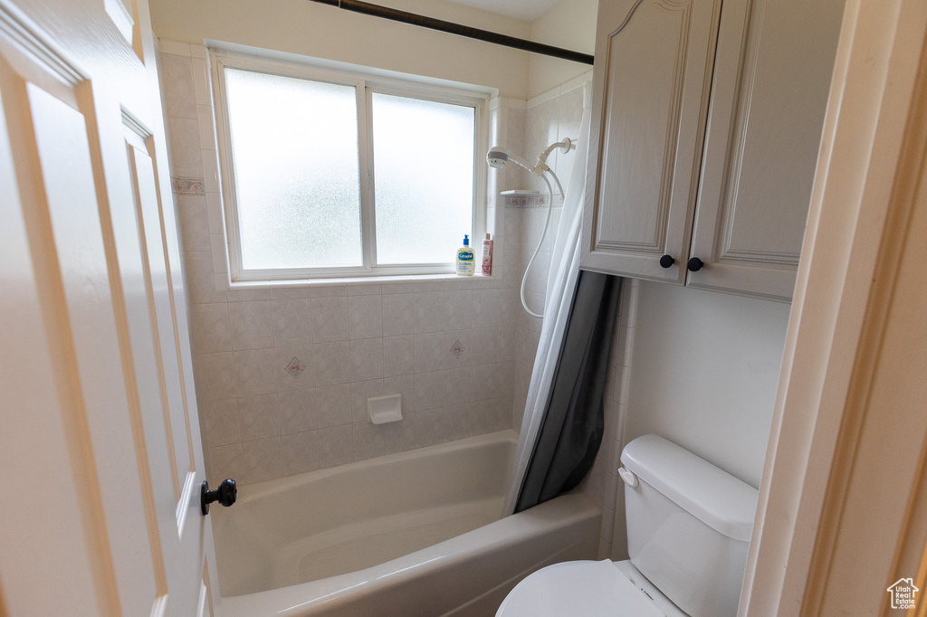 Full bathroom with toilet and shower / bath combination with curtain