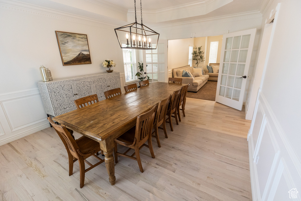 Dining area featuring plenty of natural light, crown molding, light wood-style flooring, a decorative wall, and a chandelier