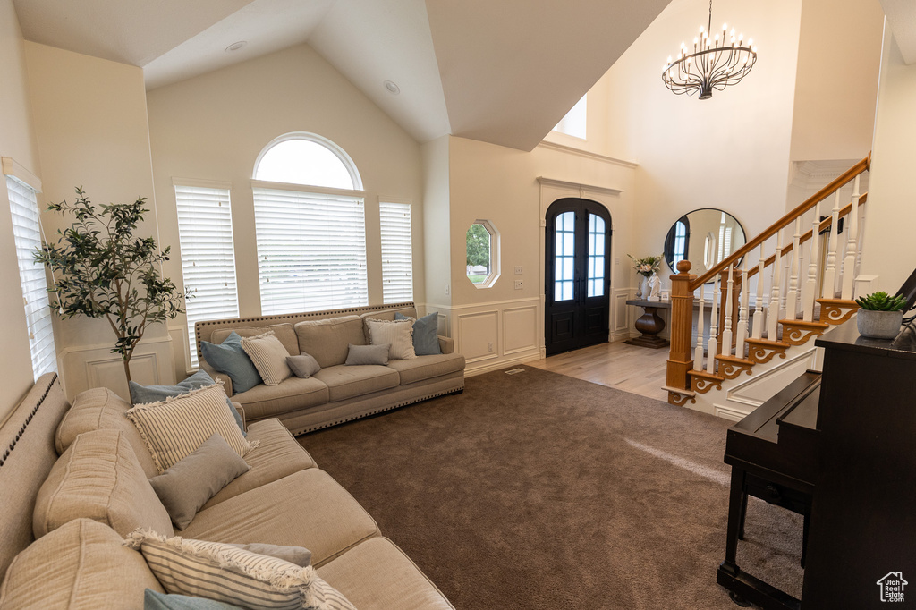 Carpeted living area featuring a decorative wall, a chandelier, high vaulted ceiling, wainscoting, and stairs
