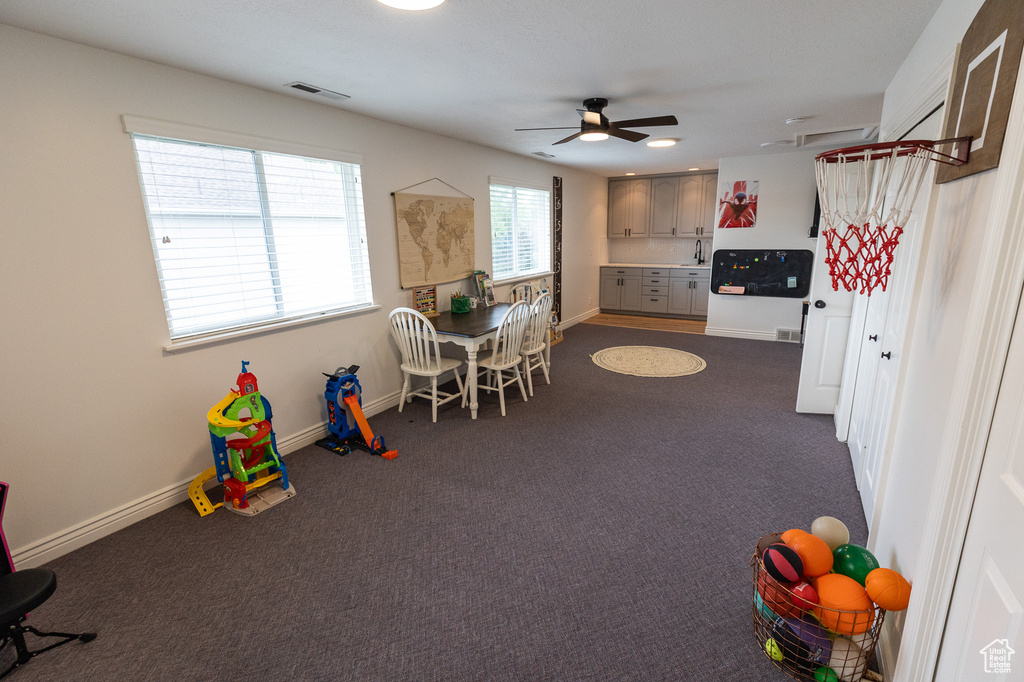Rec room with ceiling fan, dark colored carpet, baseboards, and a sink