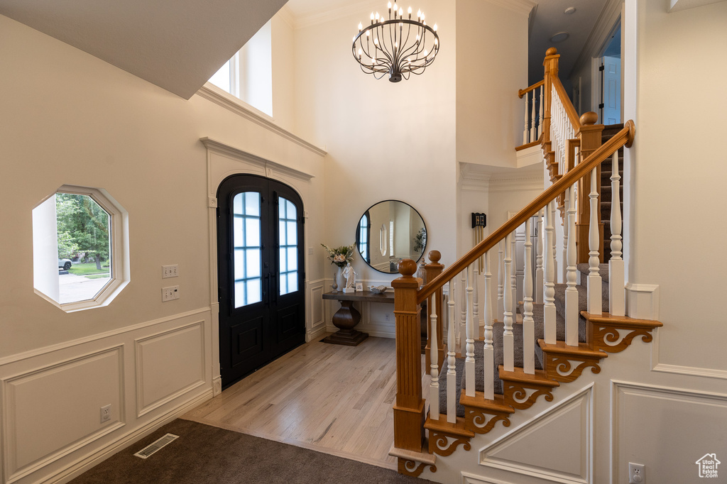 Foyer entrance with healthy amount of natural light, a decorative wall, a chandelier, stairs, and a wainscoted wall