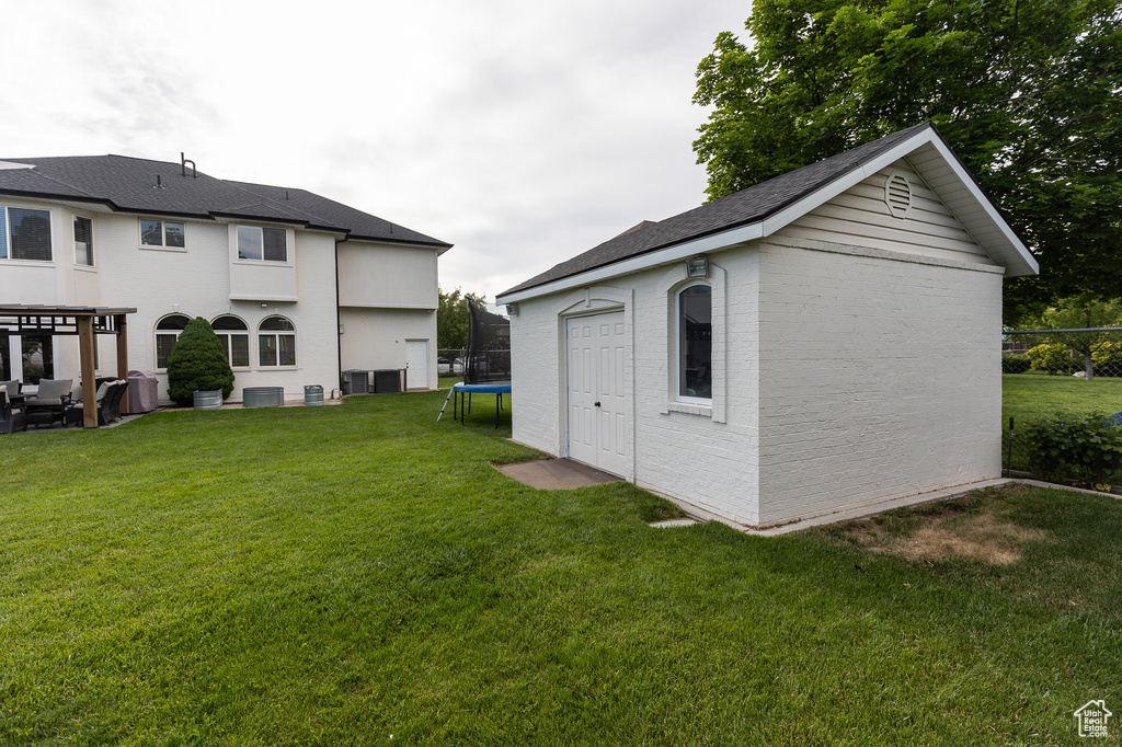 Rear view of property with a trampoline, an outdoor structure, a yard, central AC, and brick siding