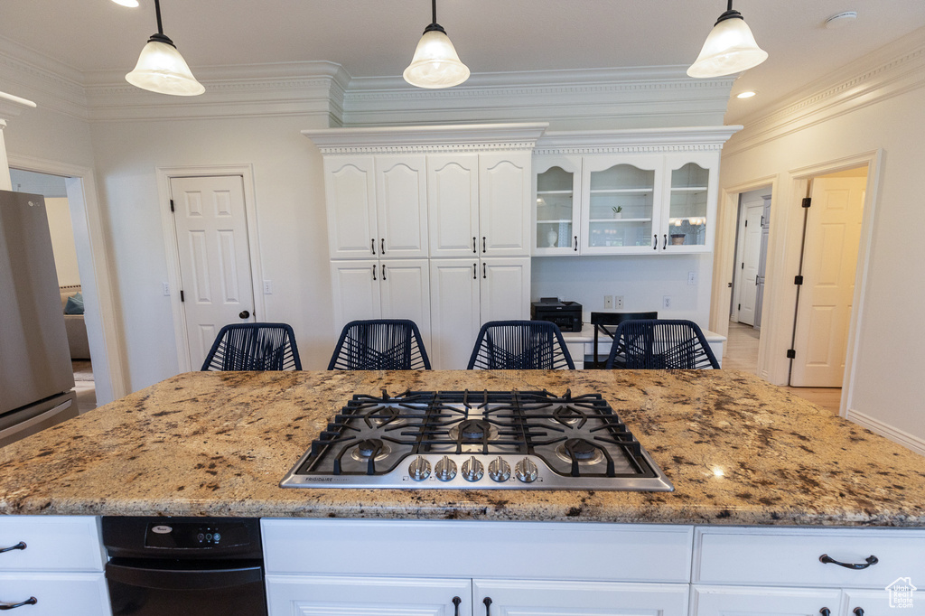 Kitchen with appliances with stainless steel finishes, ornamental molding, white cabinetry, light stone counters, and glass insert cabinets