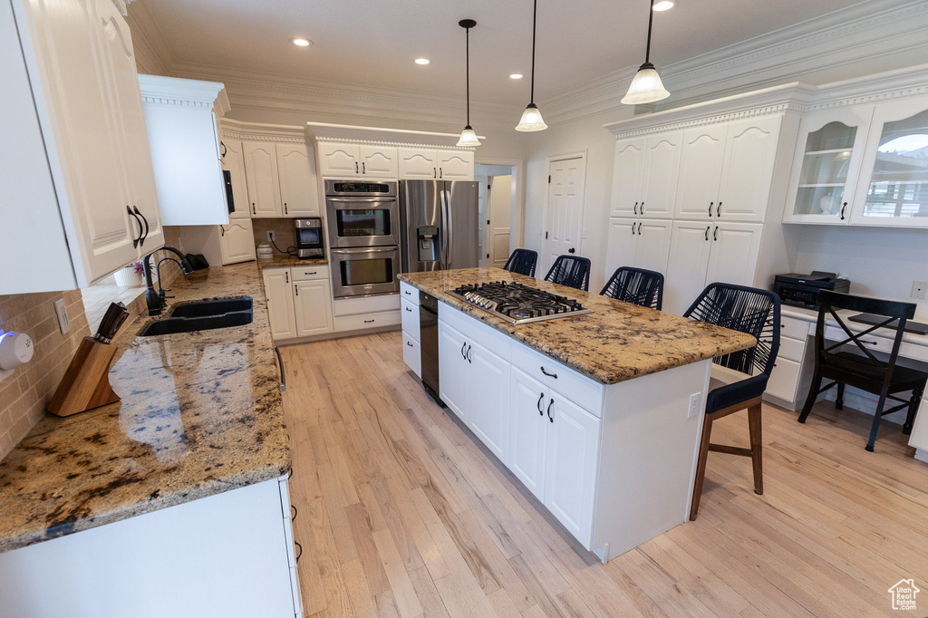 Kitchen with stainless steel appliances, a kitchen bar, white cabinetry, a center island, and a sink