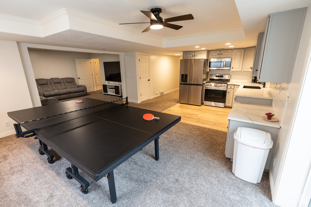 Rec room with ornamental molding, a tray ceiling, ceiling fan, baseboards, and light colored carpet