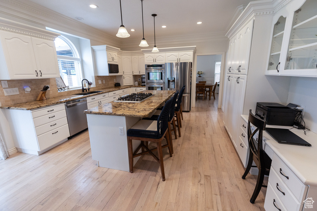 Kitchen featuring appliances with stainless steel finishes, a sink, a kitchen breakfast bar, white cabinets, and crown molding