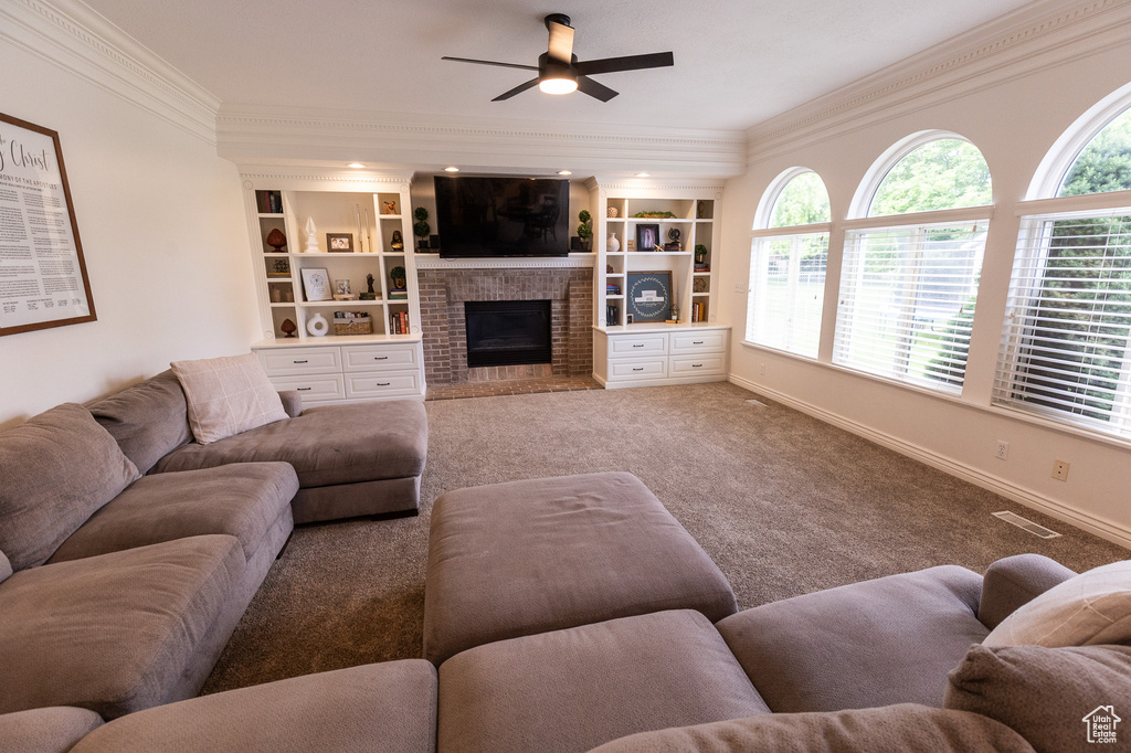 Living room with crown molding, a fireplace, ceiling fan, plenty of natural light, and carpet floors