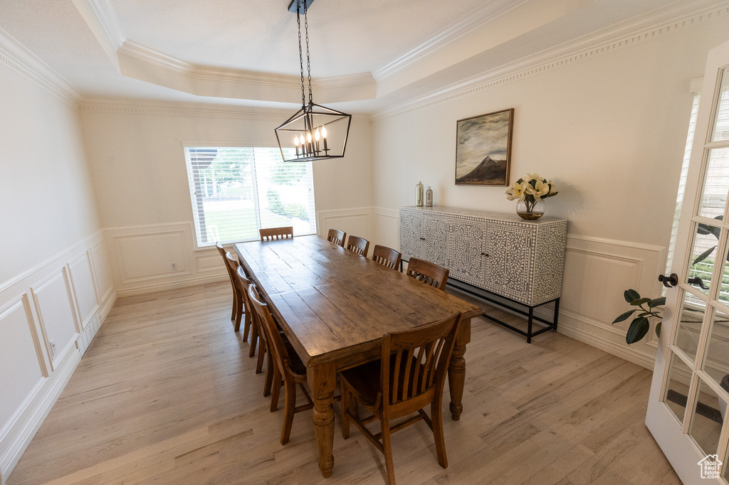 Dining room with a chandelier, a tray ceiling, light wood-style floors, a decorative wall, and ornamental molding