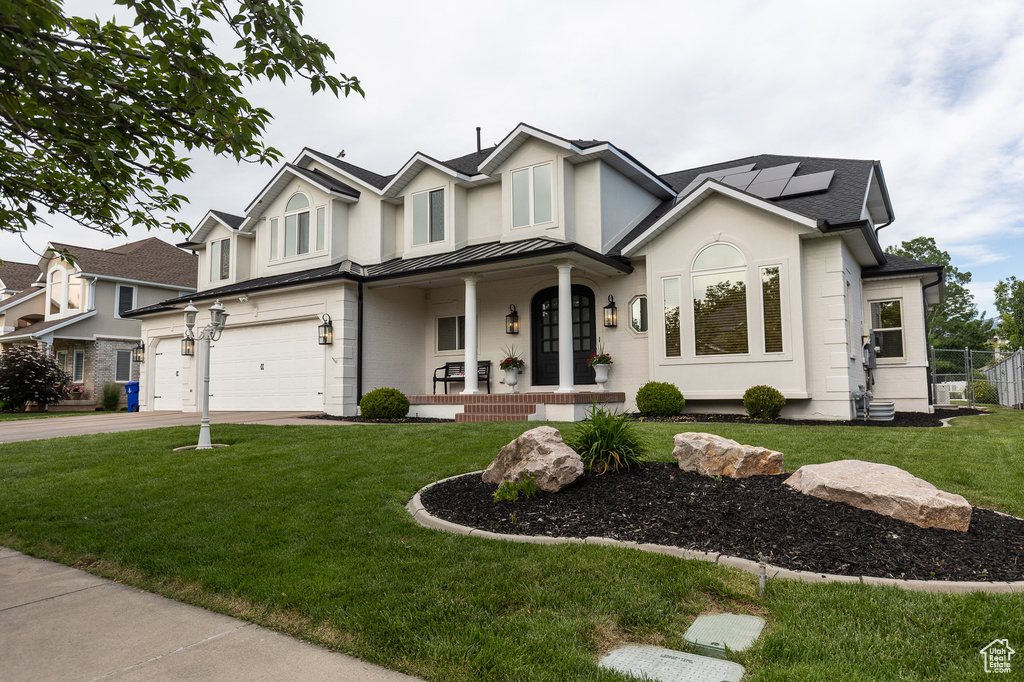 View of front of property featuring covered porch, an attached garage, a standing seam roof, solar panels, and concrete driveway