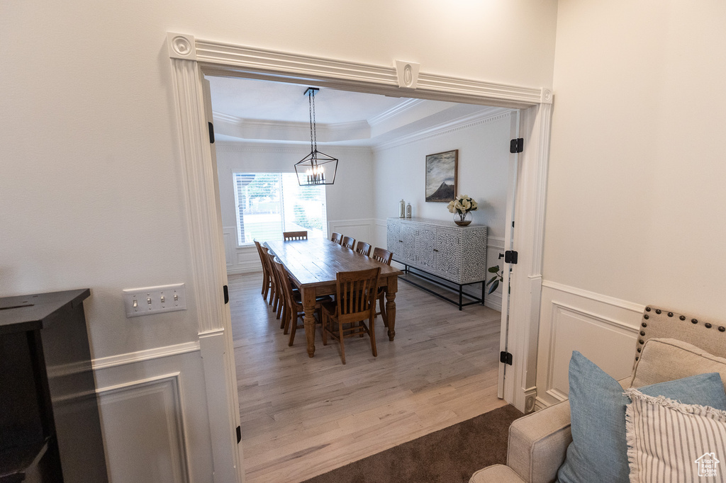 Dining space featuring ornamental molding, light wood-style floors, a chandelier, a tray ceiling, and wainscoting