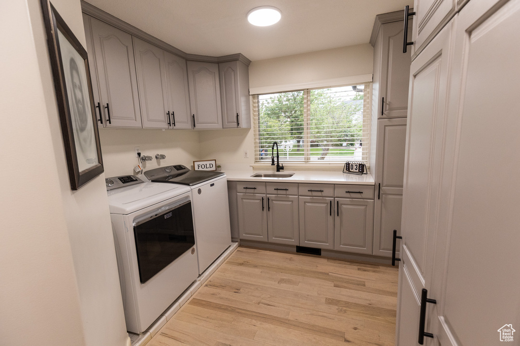 Washroom with cabinet space, washing machine and clothes dryer, and light wood-type flooring