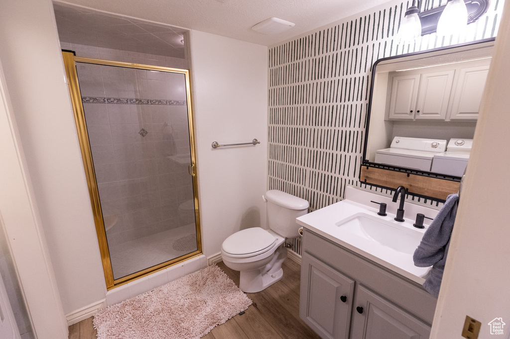 Bathroom with washer and clothes dryer, toilet, a shower stall, and wood finished floors
