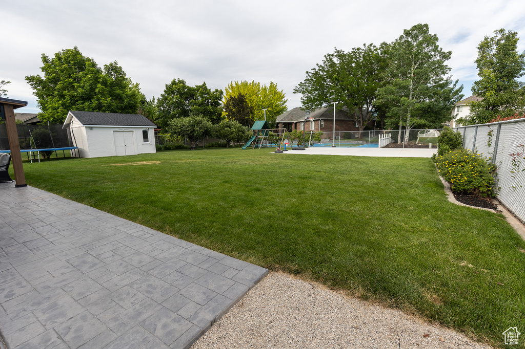 View of yard with a playground, a trampoline, an outbuilding, and a patio area
