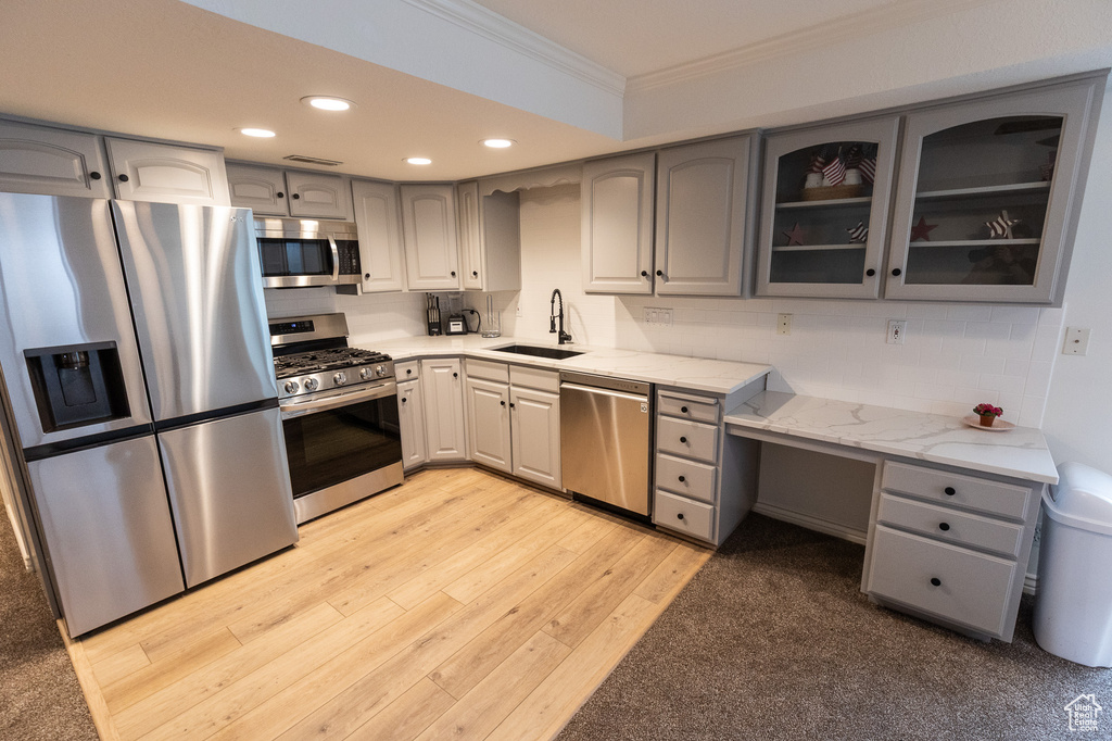 Kitchen with appliances with stainless steel finishes, a sink, gray cabinets, ornamental molding, and glass insert cabinets