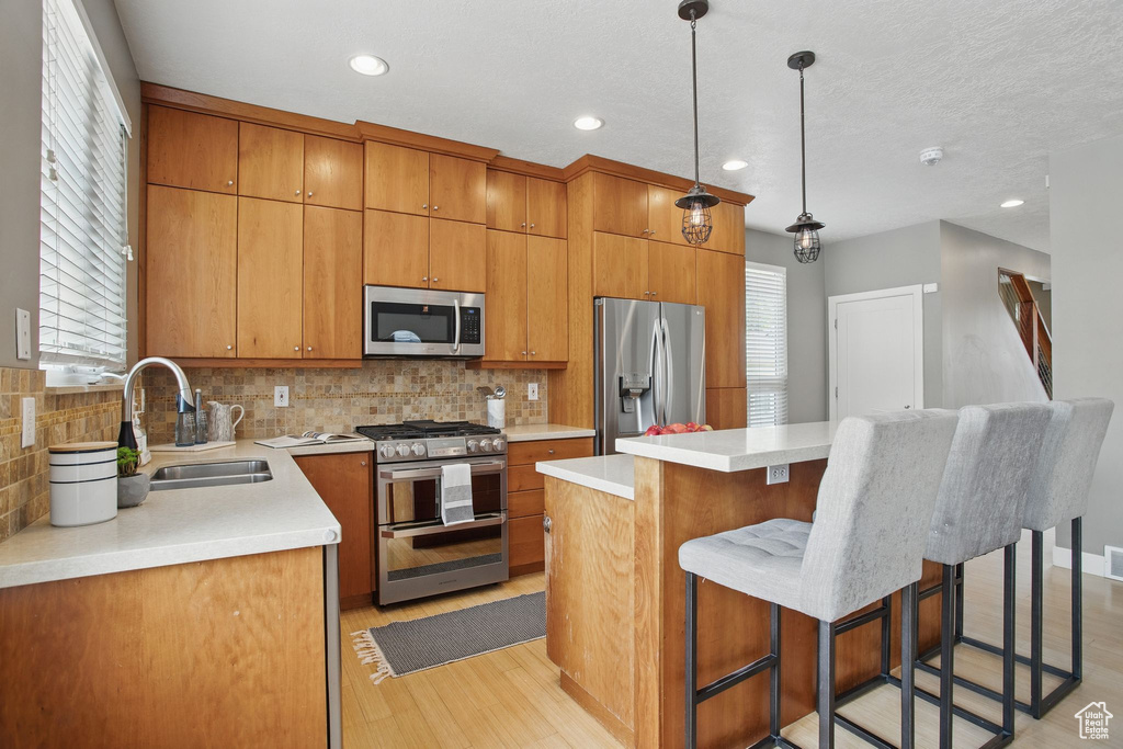 Kitchen featuring stainless steel appliances, a sink, light wood finished floors, backsplash, and recessed lighting