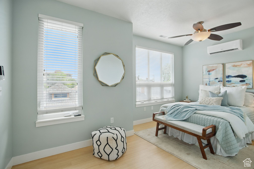 Bedroom with a wall mounted AC, wood finished floors, baseboards, and a ceiling fan