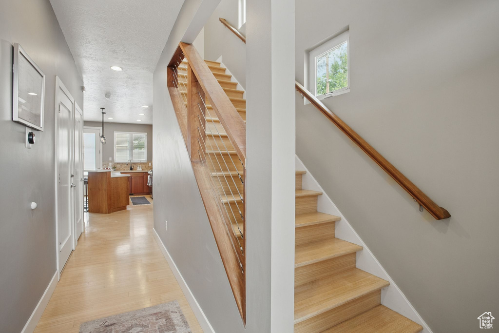Staircase with wood finished floors, baseboards, recessed lighting, and a textured ceiling