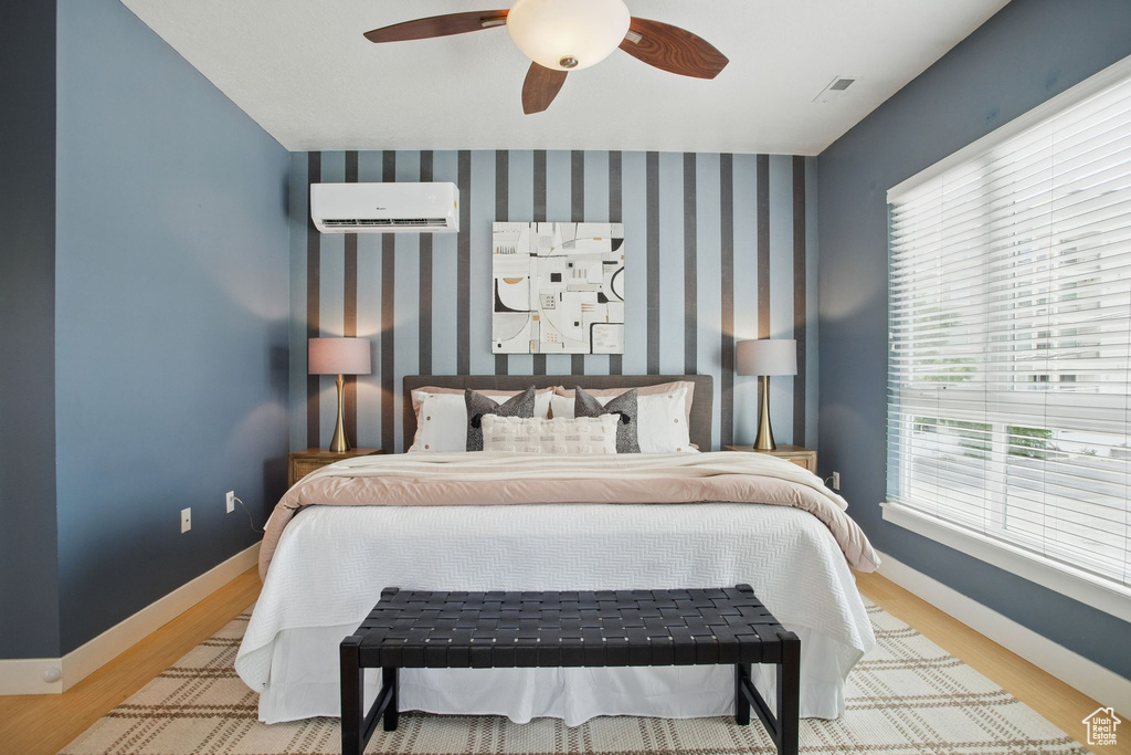Bedroom with a wall mounted air conditioner, wood finished floors, baseboards, and a ceiling fan