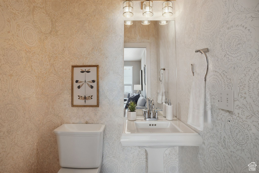 Half bathroom with toilet, a sink, and wallpapered walls