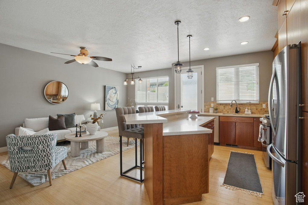 Kitchen featuring stainless steel appliances, light countertops, open floor plan, light wood finished floors, and brown cabinets