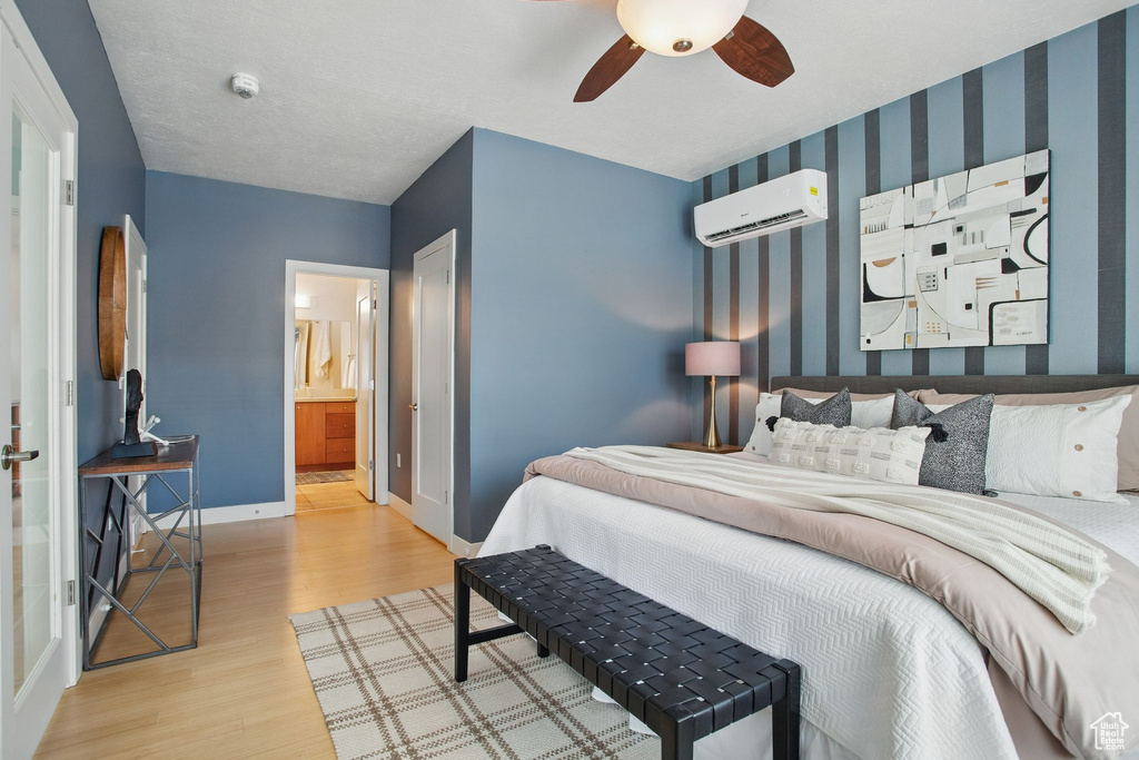 Bedroom with a wall unit AC, wood finished floors, wallpapered walls, baseboards, and ensuite bath