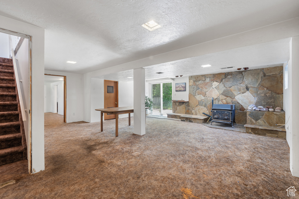 Basement featuring a textured ceiling, carpet flooring, stairway, and a wood stove