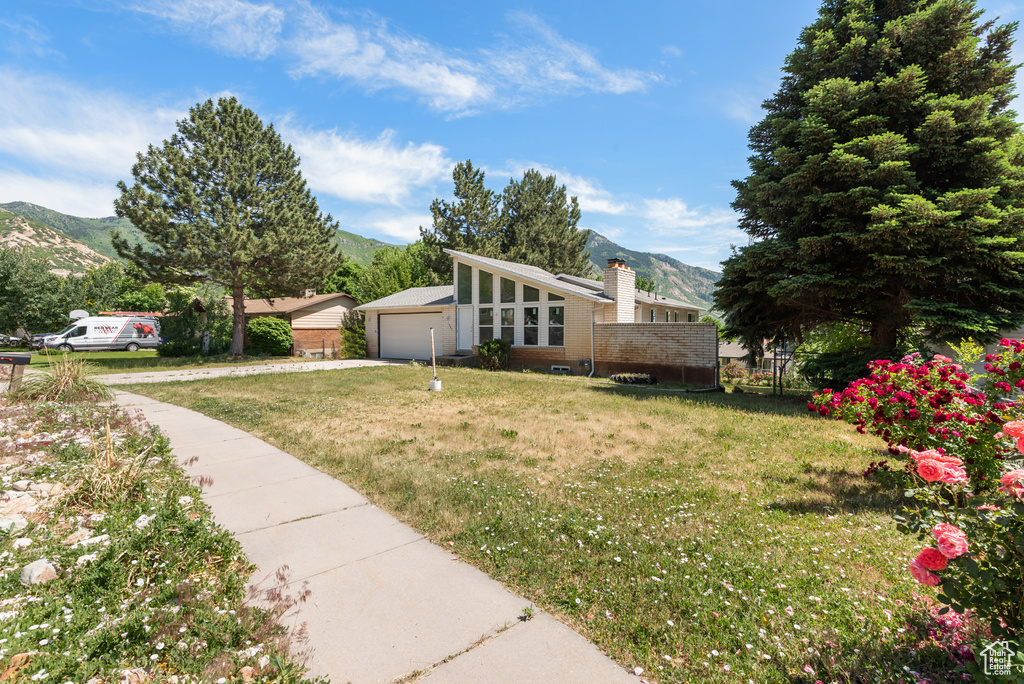 View of property exterior featuring a mountain view, brick siding, a chimney, a lawn, and concrete driveway