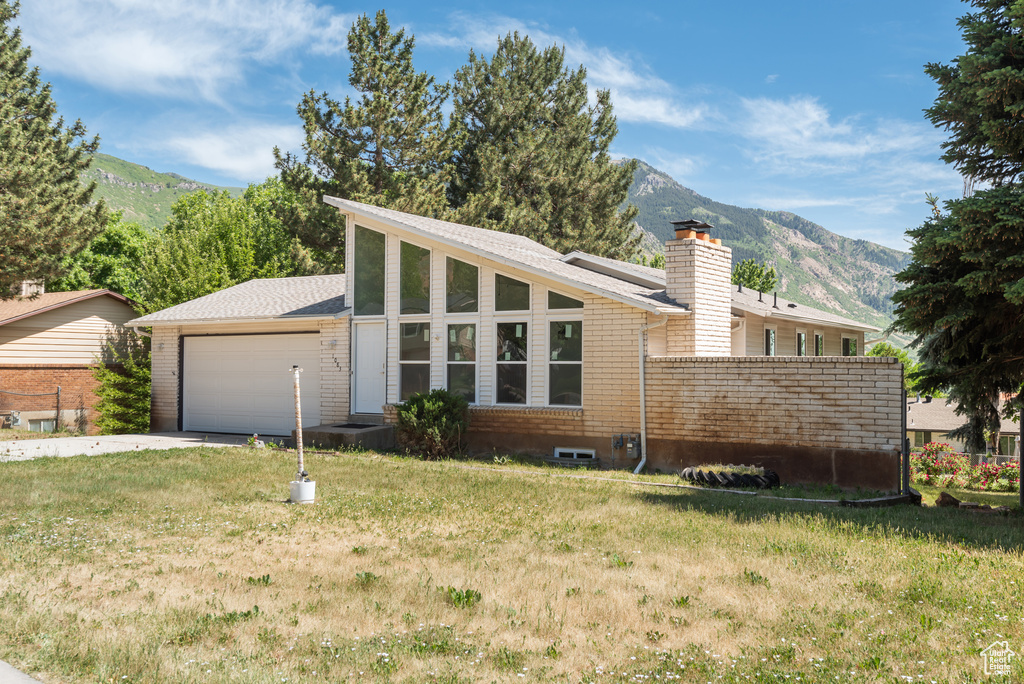 View of front of house with a chimney, a mountain view, a garage, driveway, and a front lawn