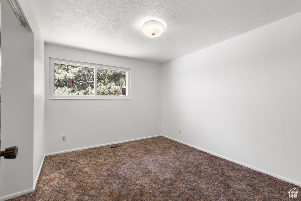 Carpeted empty room featuring a textured ceiling and baseboards