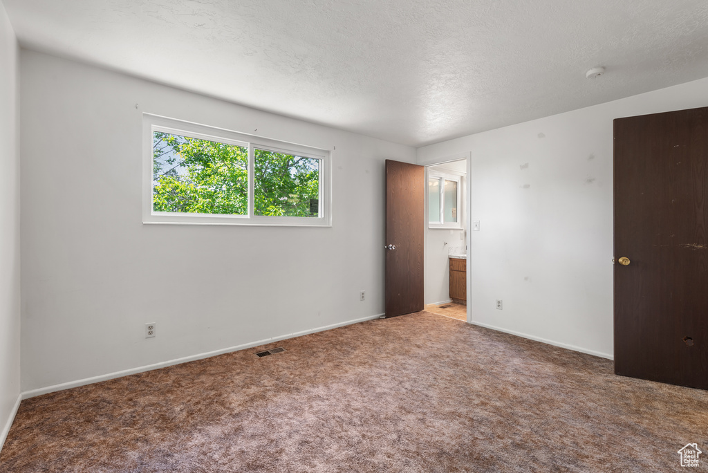 Unfurnished bedroom featuring carpet floors, baseboards, ensuite bath, and a textured ceiling
