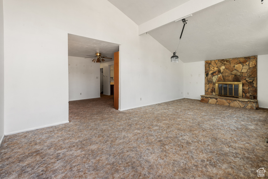 Unfurnished living room with carpet floors, high vaulted ceiling, ceiling fan, a stone fireplace, and baseboards
